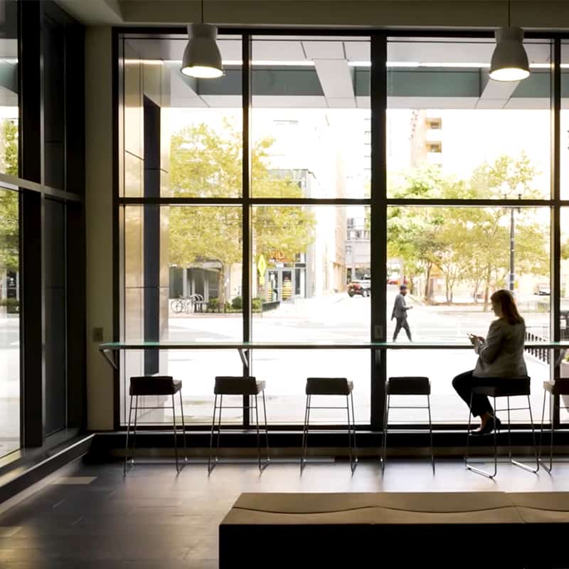 A woman sits on a barstool by a window facing the street